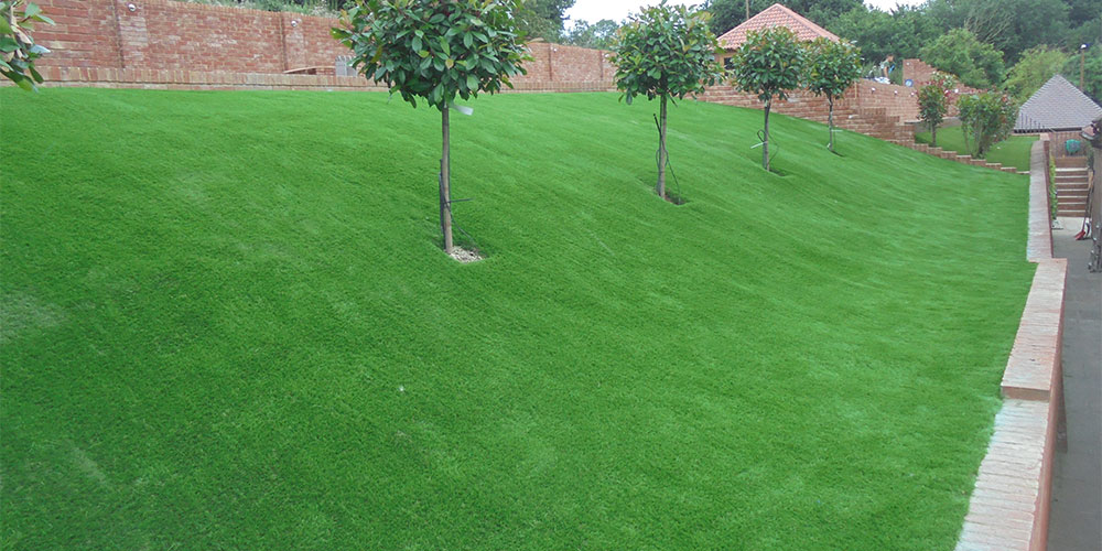 lawn slope backyard with green trees spread out in front of a brick wall