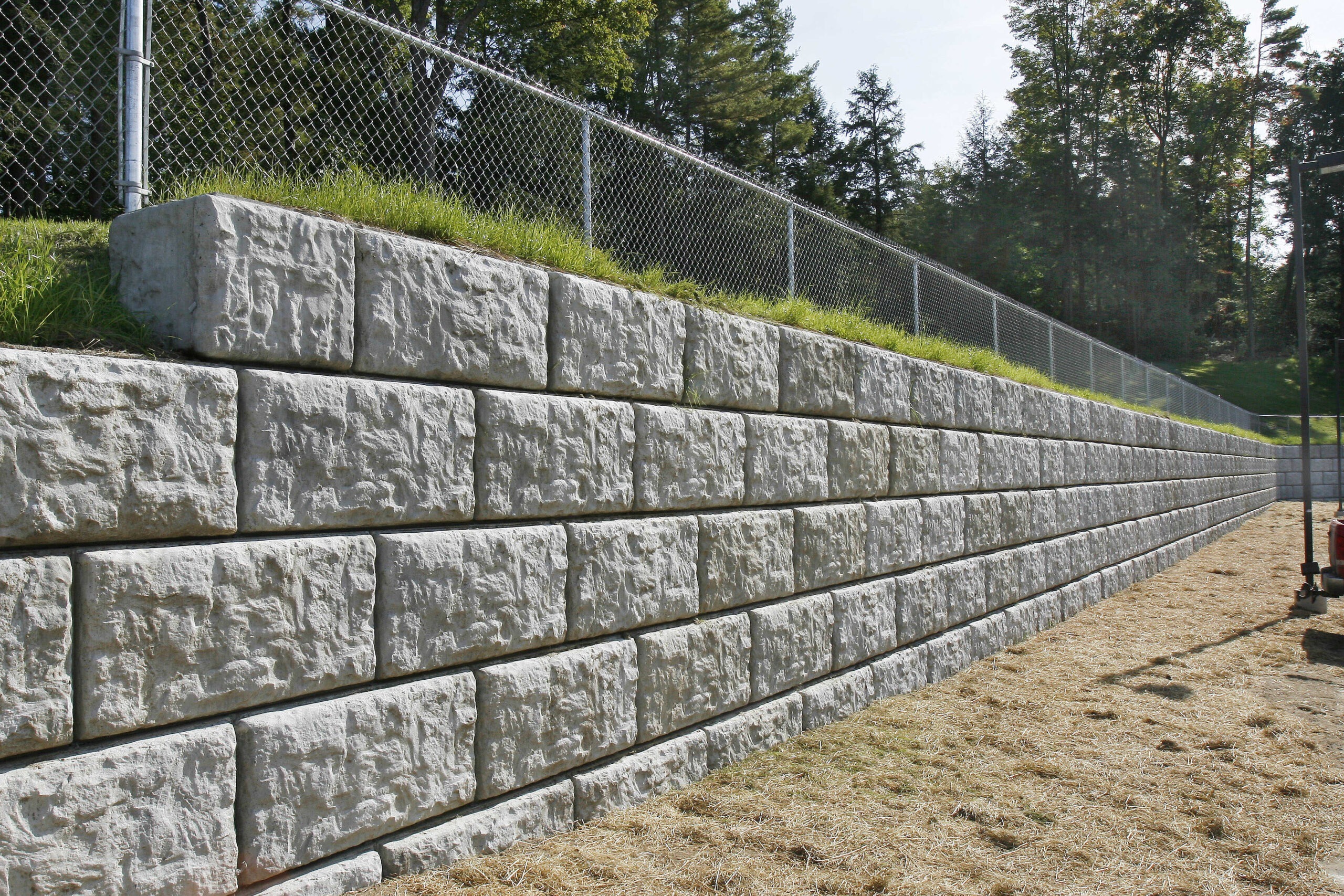gray precast concrete block retaining wall showing what is a retaining wall as a silver fence and large grass is held back